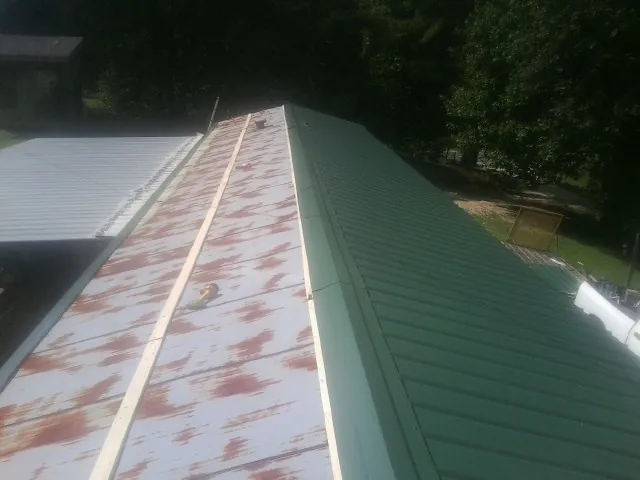 Old rusted panels beside newly installed green metal roofing — Wind Damage Roof Repair by Roofing Brothers in Junction City