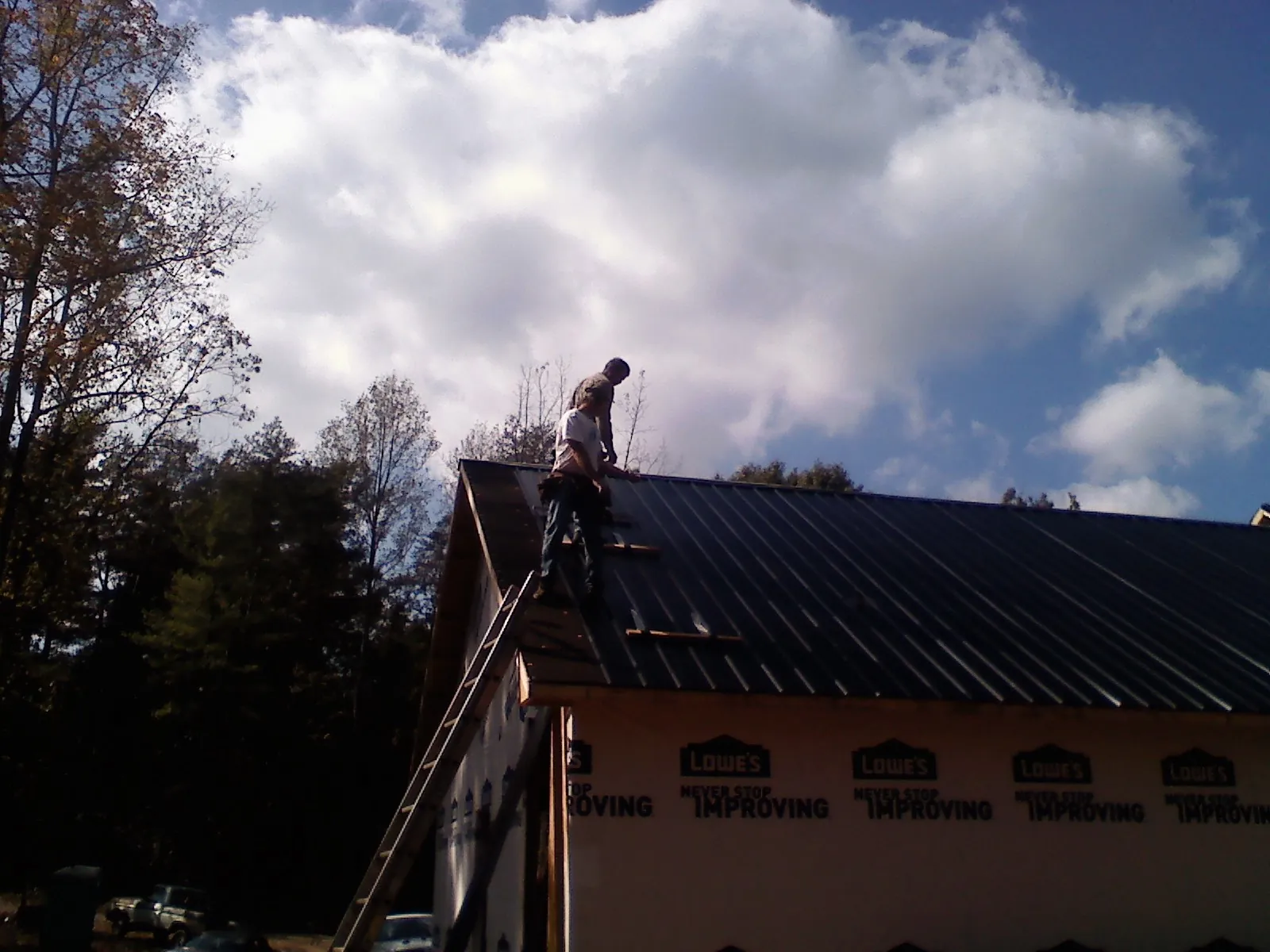 Roofer fastening dark metal panels high against a cloudy sky, from a Roof Inspection job in Junction City